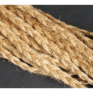 May include: Close-up of several strands of thick, natural-coloured rope. The rope is tightly woven, with a textured surface and a slightly frayed appearance. The rope is likely made of jute or hemp, and is suitable for crafts or decorative purposes.