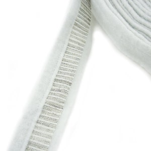 Pode incluir: Acabamento de tecido branco com uma fita de zíper prateada costurada ao longo da borda.