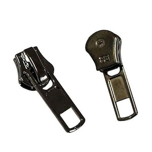 May include: Two dark grey metal zip pulls. Each pull has a rectangular opening at the bottom and a rounded top. The zip pulls are designed for use in clothing, bags, or other sewing projects.