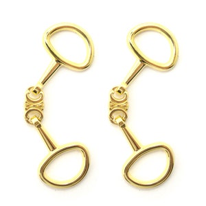 May include: Two gold-toned metal horse bit-shaped clasps with a double ring design.