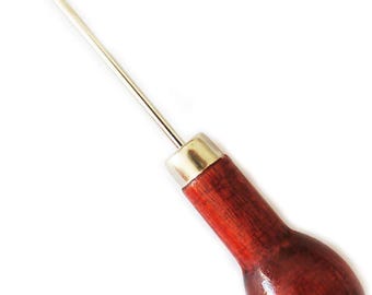 May include: A scratch awl featuring a long, pointed metal needle attached to a smooth, rounded, dark reddish-brown wooden handle. The needle is secured to the handle by a polished silver-colored metal ferrule, creating a tool for piercing materials.