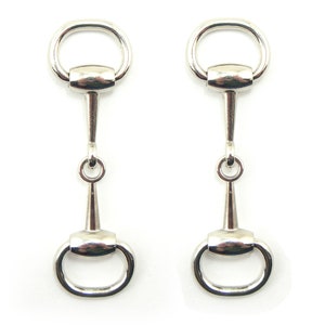May include: A pair of silver-coloured horse bit earrings. Each earring has a circular ring at the top and bottom, connected by a central post and a smaller ring. The design is symmetrical and detailed, with a polished finish.