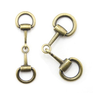 May include: Two antique gold-toned metal horse bit buckles. Each buckle has a round ring on one end and a D-shaped ring on the other end.