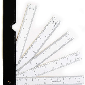 May include: A white plastic architectural scale ruler fan with multiple folding blades, each featuring various ratio markings and black numerical scales. The blades are attached to a black protective sleeve with a metal rivet at the base.