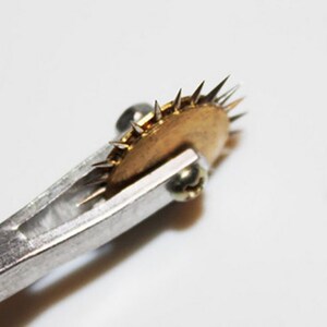 May include: A close-up of a silver tool with a brass wheel with sharp points. The wheel is attached to the tool with a screw.