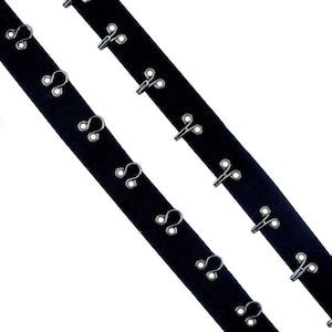May include: Two strips of black hook and eye tape, angled diagonally. Each strip features evenly spaced silver metal hooks and eyes, used for fastening garments. The background is white.