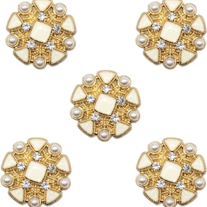 May include: Five gold buttons with an off-white square centre, encircled by pearls, clear crystals, and triangular off-white details. These ornate buttons have a vintage design, suitable for embellishing clothing or accessories.