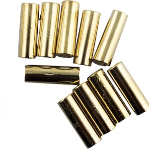 Pode incluir: Uma coleção de nove contas cilíndricas de metal em tom dourado dispostas em dois grupos. As contas têm uma superfície lisa e reflexiva com um centro oco, projetadas para serem enfiadas em cordão ou arame para joalharia e artesanato.