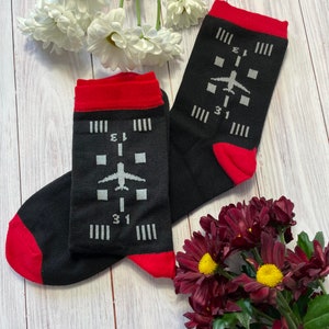 May include: A pair of black socks with red trim. One sock has a white airplane graphic and the text "31" and "E1" on it. The other sock has the same design but with the text "31" and "E1" reversed.