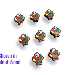 May include: A collection of seven small, wooden turkey-shaped ornaments. Each ornament features a brown body, a red wattle, and a colorful tail with yellow, orange, and green accents. The text "Shown in Walnut Wood" is displayed in purple.