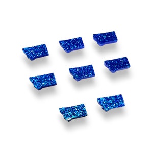 May include: Eight blue glitter state of Montana shaped stickers. The stickers are scattered on a white background.