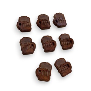 May include: Seven small, dark brown wooden beer mug shapes with carved details. The mugs are arranged on a white background, each with a handle and a foamy top. The wood grain is visible, adding texture to the miniature beer steins.
