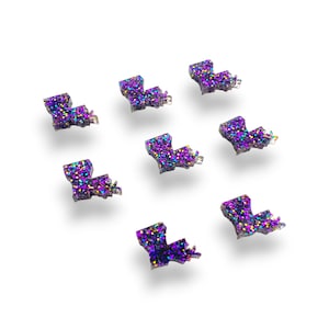 May include: Eight purple and iridescent glitter Louisiana state outline shapes on a white background.