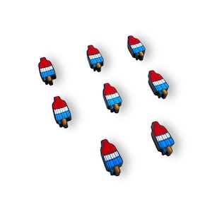 May include: A collection of eight popsicle charms. Each charm features a red top, white and blue stripes, and a brown stick. The charms are scattered on a white background.