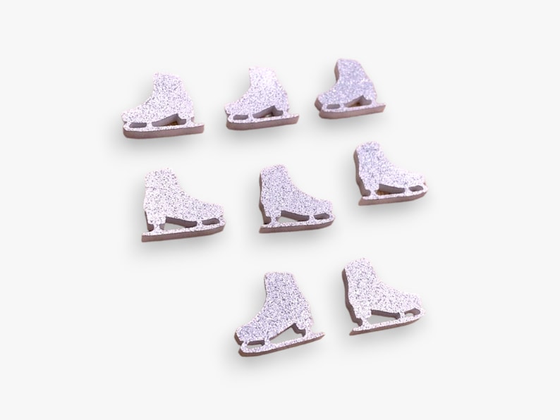 May include: Eight small, flat, die-cut ice skate shapes arranged in a cluster. Each skate features a silver glitter finish on the upper portion and a brown base, showcasing the blade and boot structure in a simple, uniform, and decorative design.