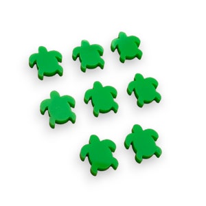 May include: Seven small, bright green turtle-shaped embellishments are scattered on a white background. Each turtle has a distinct shape with a head, four flippers, and a shell. The turtles are evenly spaced and appear to be made of a solid material.