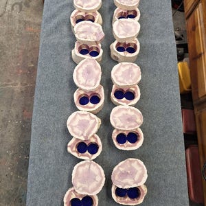 May include: A top-down view of two columns of wooden, circular, decorative boxes. Each box is made from a light-colored wood with a purple-hued center and a deep blue interior. The boxes are arranged on a gray surface.