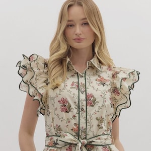 以下が含まれることがあります： クリーム色の花柄ワンピース。ウエストにリボン、袖にフリルが付いています。ボタンダウンフロント、スカラップヘム、グリーンのトリムが特徴です。花柄にはピンクとグリーンの花が含まれています。