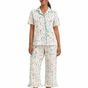 Puede incluir: Conjunto de pijama blanco con un estampado colorido de varios objetos y ribete verde. La parte superior de manga corta y los pantalones cortos tienen un dobladillo con volantes. El estampado incluye detalles en rosa, azul y amarillo.