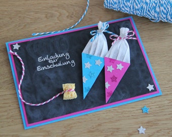 May include: A black chalkboard card with a blue and pink border. The card says "Einladung zur Einschulung" which translates to "Invitation to School Enrollment". There are two paper cones decorated with glitter and stars, and a yellow sponge tied with twine.