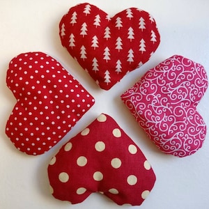 May include: Four red heart-shaped cushions with different patterns. One cushion has a white polka dot pattern, one has a white tree pattern, one has a white swirl pattern, and one has a larger white polka dot pattern.