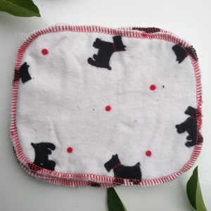 May include: A set of six white cotton washcloths with red stitched edges and a black silhouette of a dog printed on each cloth.