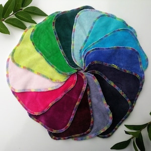 Könnte beinhalten: Ein Set mit 12 bunten wiederverwendbaren Abschminkpads mit gewelltem Rand. Die Pads sind in einem Kreis angeordnet, wobei die Farben von Hellblau bis Dunkelgrün reichen.