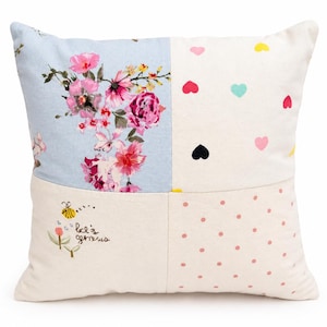 May include: Square cushion with a patchwork design. One section displays a floral print with pink and red flowers on a light blue backdrop. Other sections feature hearts, polka dots, and a bee with the text "let's grow".