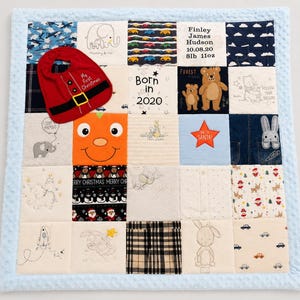 May include: A patchwork baby quilt with a light blue border. The quilt features various fabric squares with images of cars, elephants, bears, and a pumpkin face. A red bib with a Santa design is on top. The quilt also has the text "Born in 2020".