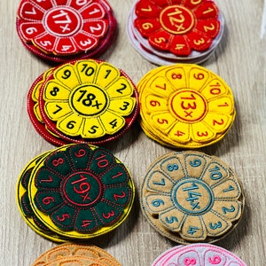 May include: A set of ten colorful felt circles with embroidered numbers and multiplication symbols. Each circle has a different color and features a different multiplication problem. The circles are arranged in two rows of five.