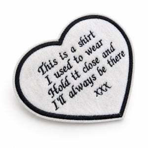 Pode incluir: Um patch em forma de coração branco com uma borda preta. O patch tem texto bordado que diz: "This is a shirt I used to wear Hold it close and I'll always be there XXX."