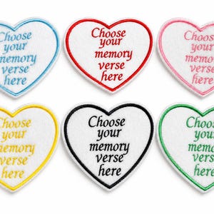 Peut inclure: Six écussons en forme de cœur avec texte brodé. Chaque écusson a un centre blanc et un bord coloré : bleu, rouge, rose, jaune, noir et vert. Le texte "Choose your memory verse here" est brodé dans une couleur assortie.
