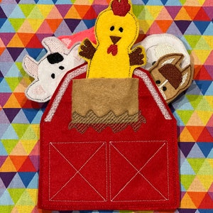 Peut inclure: Une grange rouge en feutre avec un fenil beige et trois marionnettes de doigts d'animaux de la ferme : un poulet jaune, une vache blanche &agrave; taches noires et un cheval marron. Les marionnettes sont en feutre et brod&eacute;es de d&eacute;tails. Le fond est un motif g&eacute;om&eacute;trique color&eacute;.