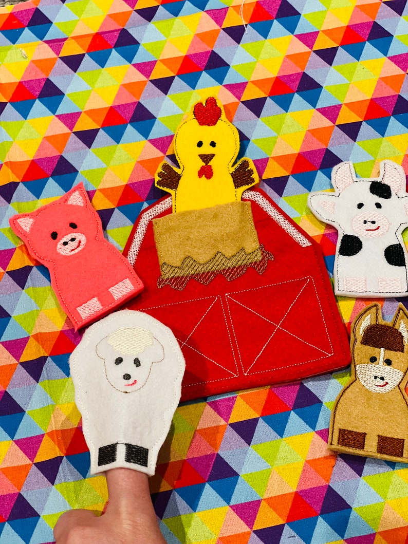 Peut inclure: Un ensemble de marionnettes &agrave; doigts en feutre repr&eacute;sentant une ferme : une grange rouge, un coq jaune, un cochon rose, un mouton blanc, une vache noire et blanche et un cheval brun. Fond color&eacute;.