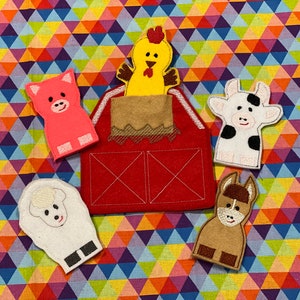 Peut inclure: Une grange en feutre rouge avec un toit marron, entour&eacute;e de cinq marionnettes &agrave; doigts : un cochon rose, un poulet jaune, une vache blanche, un mouton blanc et un &acirc;ne marron. Le fond est un motif g&eacute;om&eacute;trique color&eacute;.