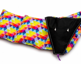 May include: A brightly coloured baby pillow with a geometric pattern and a black section. The pillow features a vibrant array of colours including red, yellow, blue, and purple triangles. The black section has two diamond-shaped cutouts.