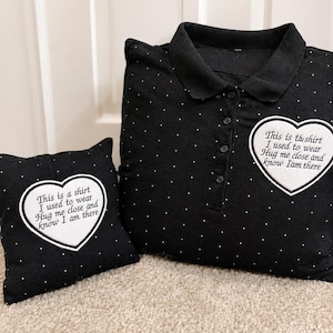 Può includere: Due cuscini neri a pois, uno a forma di camicia, con testo ricamato bianco all'interno di un contorno a forma di cuore. Il testo recita: "This is a shirt I used to wear Hug me close and Know I am there."