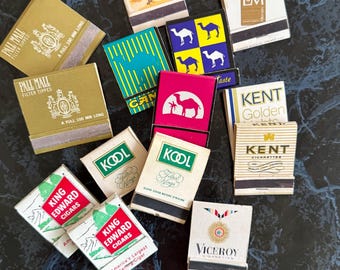 May include: A collection of vintage matchbooks featuring various brands. The matchbooks display logos and text, including "Camel," "Pall Mall," "King Edward Cigars," and "Kool." The color palette includes gold, red, green, and blue.