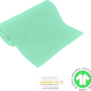Könnte beinhalten: Eine Rolle hellgrünen Stoffes mit den Zertifizierungen Oeko-Tex Standard 100 und Global Organic Textile Standard (GOTS).