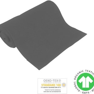 Könnte beinhalten: Eine Rolle dunkelgrauer Stoff mit dem Oeko-Tex Standard 100 Zertifizierungslabel und dem Global Organic Textile Standard (GOTS) Logo.