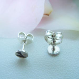May include: A pair of silver stud earrings with butterfly backs. The flat, circular front faces are polished and reflective. The back of one earring is clearly stamped with the hallmark 925, indicating sterling silver composition.