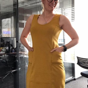 May include: A mustard yellow sleeveless dress with two pockets on the front. The dress is fitted and has a scoop neckline.