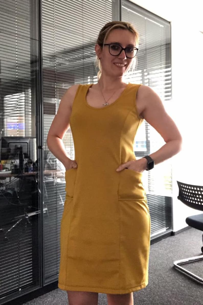 May include: A mustard yellow sleeveless dress with two pockets on the front. The dress is fitted and has a scoop neckline.