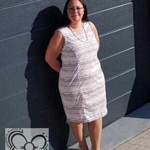 May include: A woman wearing a white and gray striped sleeveless dress with a pearl necklace and white shoes. She is standing in front of a gray garage door.