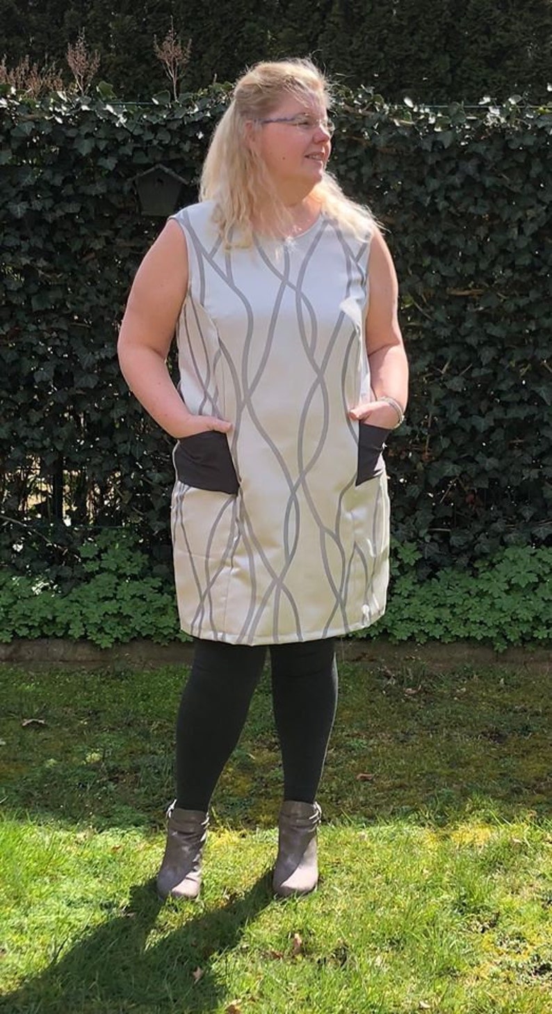 May include: A woman wearing a sleeveless dress with a gray and white abstract pattern. The dress has two black pockets on the front. She is wearing black leggings and gray ankle boots.