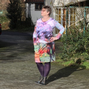 May include: A woman wearing a colourful long-sleeved dress with a floral and animal print. She is wearing purple tights and black ankle boots.
