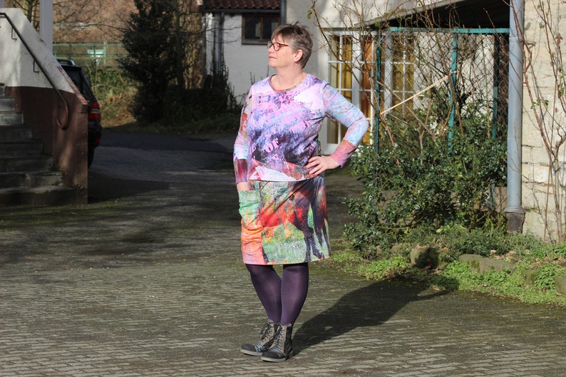 May include: A woman wearing a colourful long-sleeved dress with a floral and animal print. She is wearing purple tights and black ankle boots.