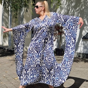 Könnte beinhalten: Ein fließendes, langes Kleid mit blau-weißem Ikat-Muster. Das Kleid hat einen V-Ausschnitt und weite Ärmel. Das Model trägt beige Absätze.