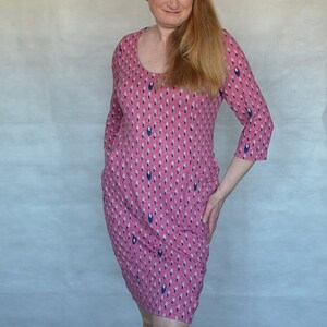 May include: A woman wearing a pink dress with a blue and white pattern. The dress has a scoop neck and three-quarter sleeves.