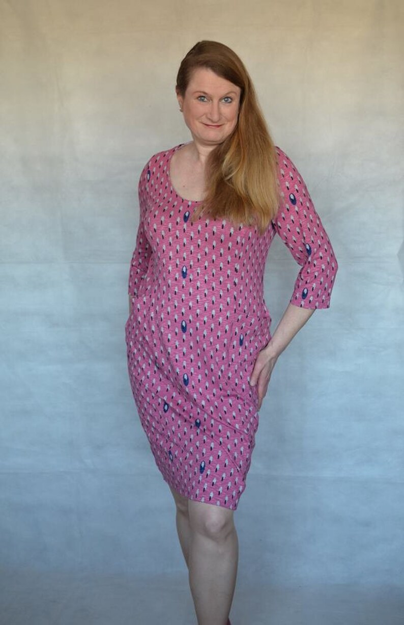 May include: A woman wearing a pink dress with a blue and white pattern. The dress has a scoop neck and three-quarter sleeves.